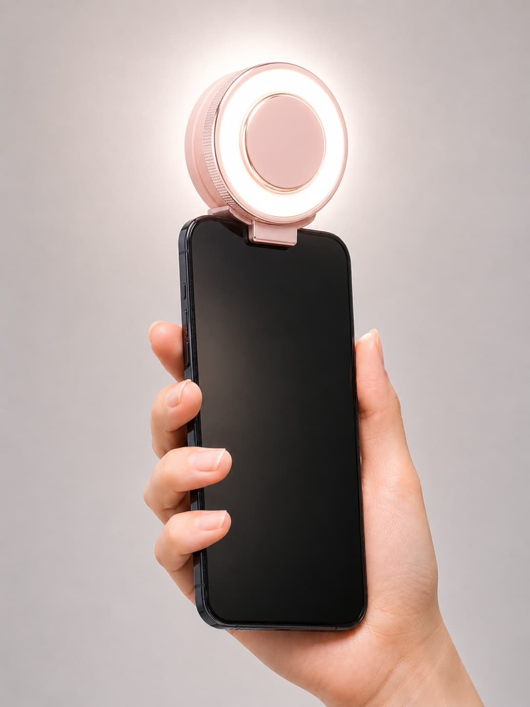 Close-up of a hand holding a smartphone with the pink MagCool fan magnetically attached, showcasing the active adjustable LED ring light for fill lighting.