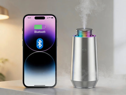 Silver StellTails GS-01 smart car diffuser dispensing visible cold-air mist next to an iPhone displaying Bluetooth app control for custom fragrance settings.
